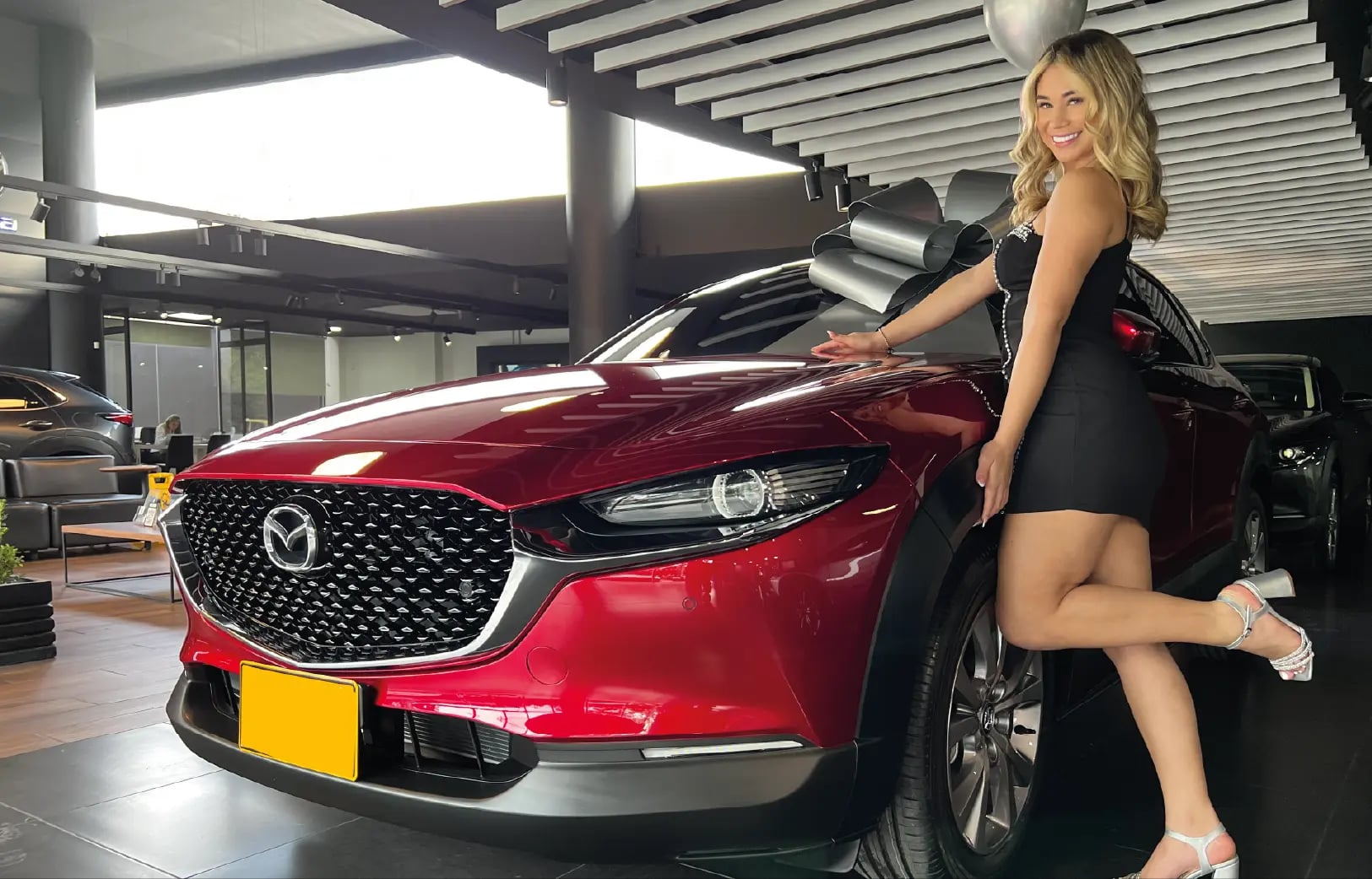 Modelo de Models 1A junto a Mazda rojo con moño plateado en concesionario